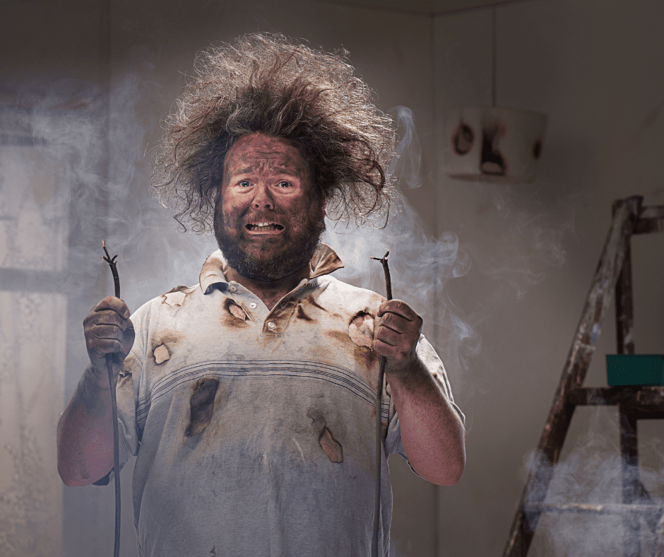 A man with frizzy hair and dirty face holding two severed wires that have burned